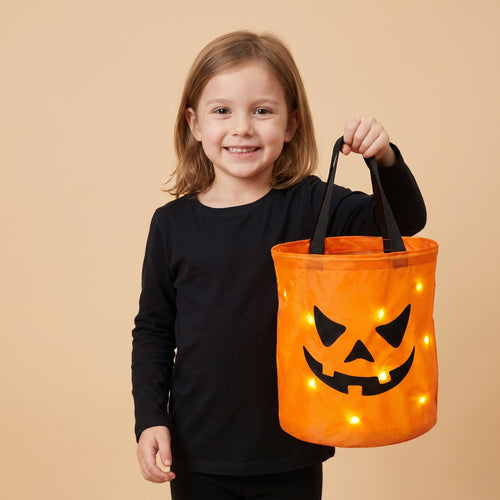 Smiling girl holding the glowing pumpkin candy bucket