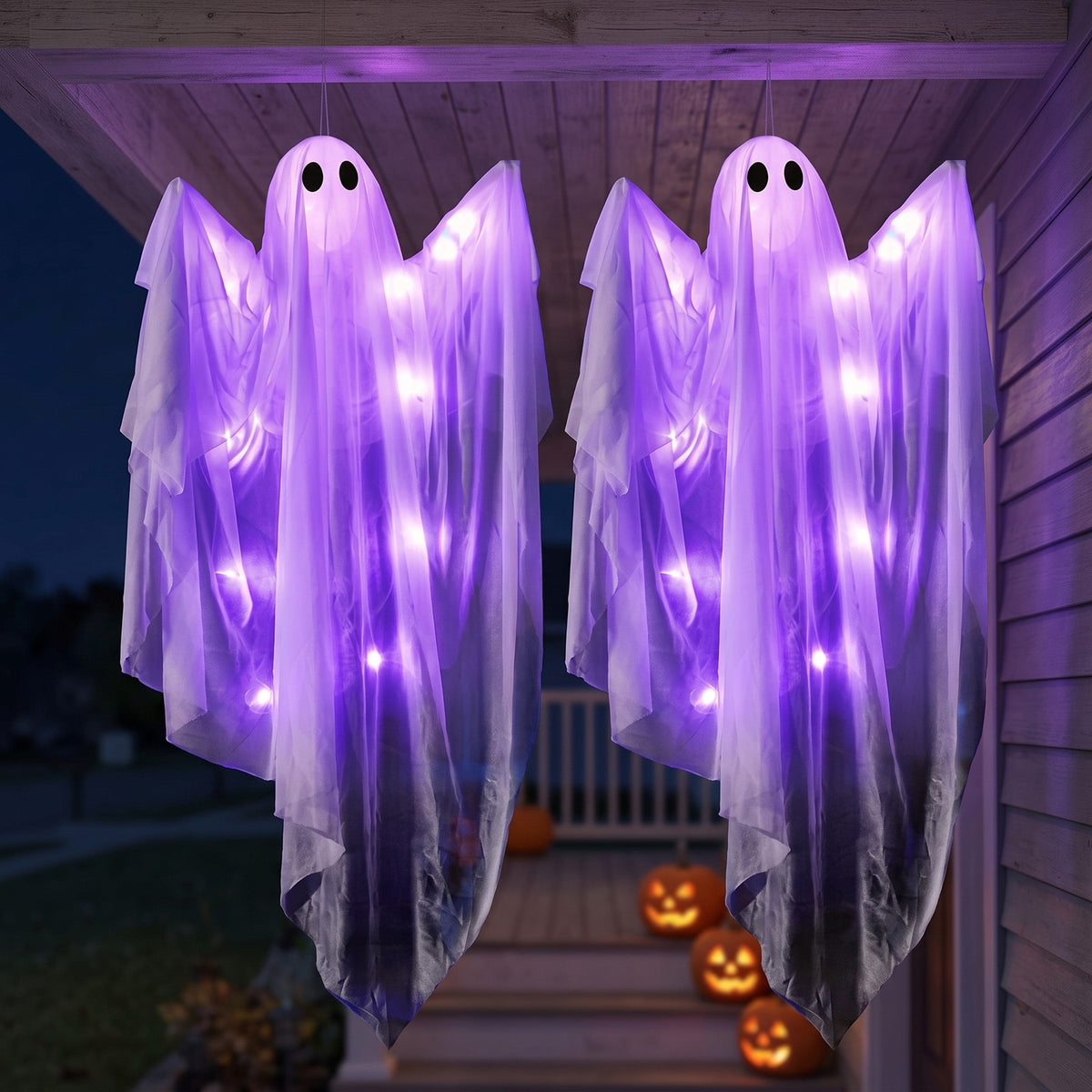 Two sheer white hanging ghosts glowing purple under a porch roof at night, jack-o'-lanterns on the steps