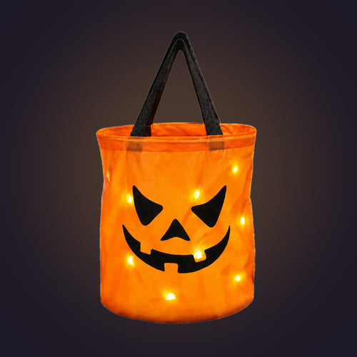 Orange light-up pumpkin candy bucket with black handles, glowing, on a dark background